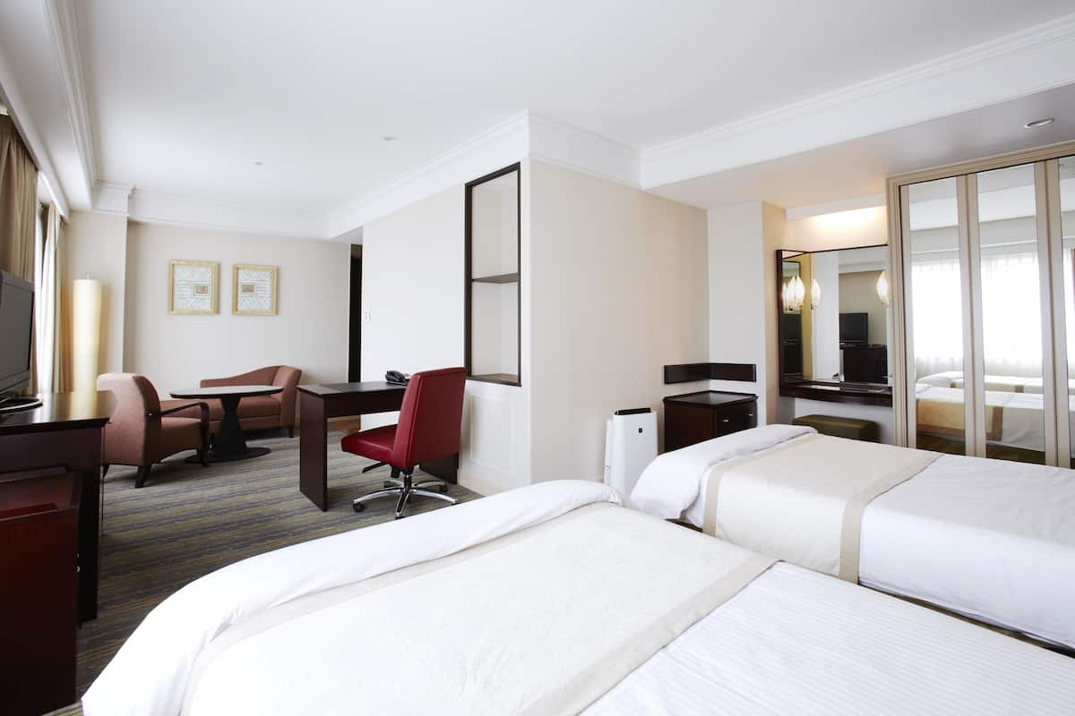 Ein Hotelzimmer mit zwei Betten, einem Schreibtisch, einem Sessel, einem Fernseher und einem großen Spiegel.
