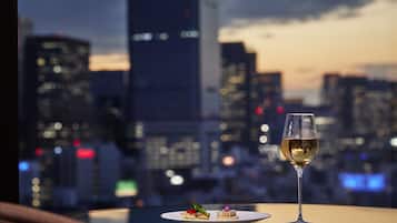 Una mesa con una copa de vino y un plato de comida, con vistas a un paisaje urbano al fondo.