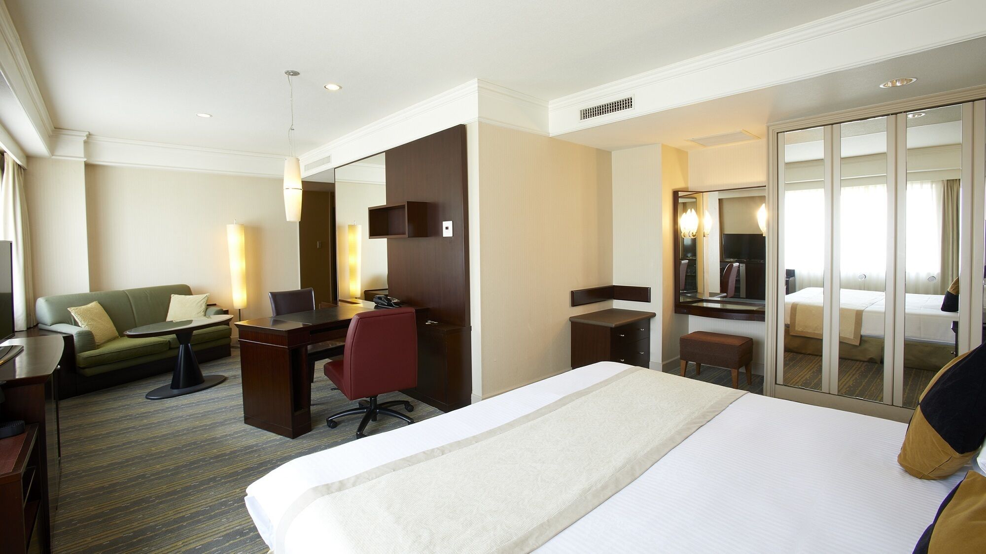 Ein Hotelzimmer mit Bett, Schreibtisch, Sessel, Sofa, Spiegel und Kleiderschrank.