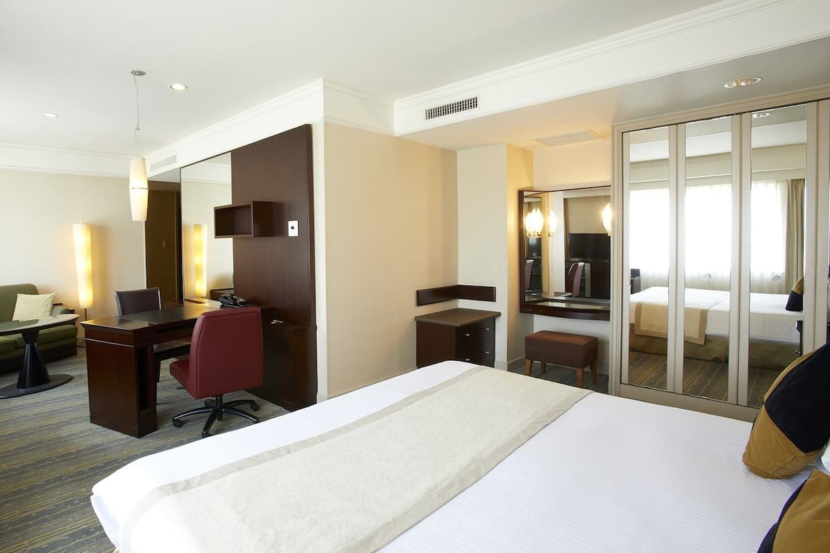 A hotel room with a bed, a desk, a chair, a sofa, a mirror, and a wardrobe.