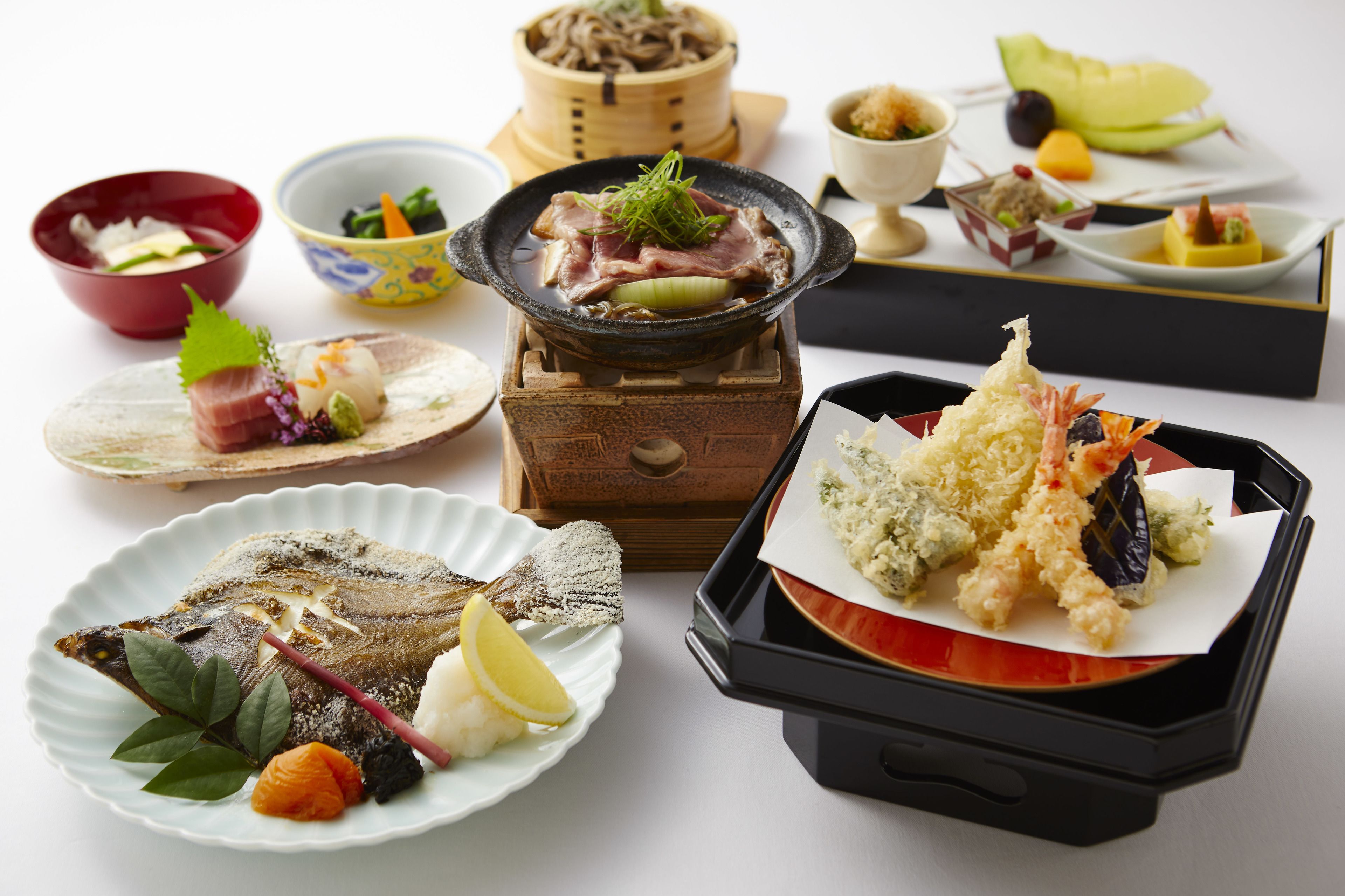 A variety of Japanese dishes including sushi, tempura, and other appetizers arranged on a table.