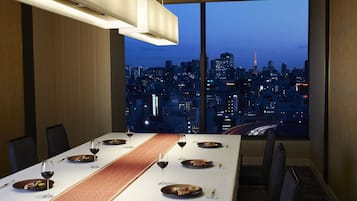 Un comedor con vistas a la ciudad, una larga mesa dispuesta para cuatro personas y una iluminación moderna.