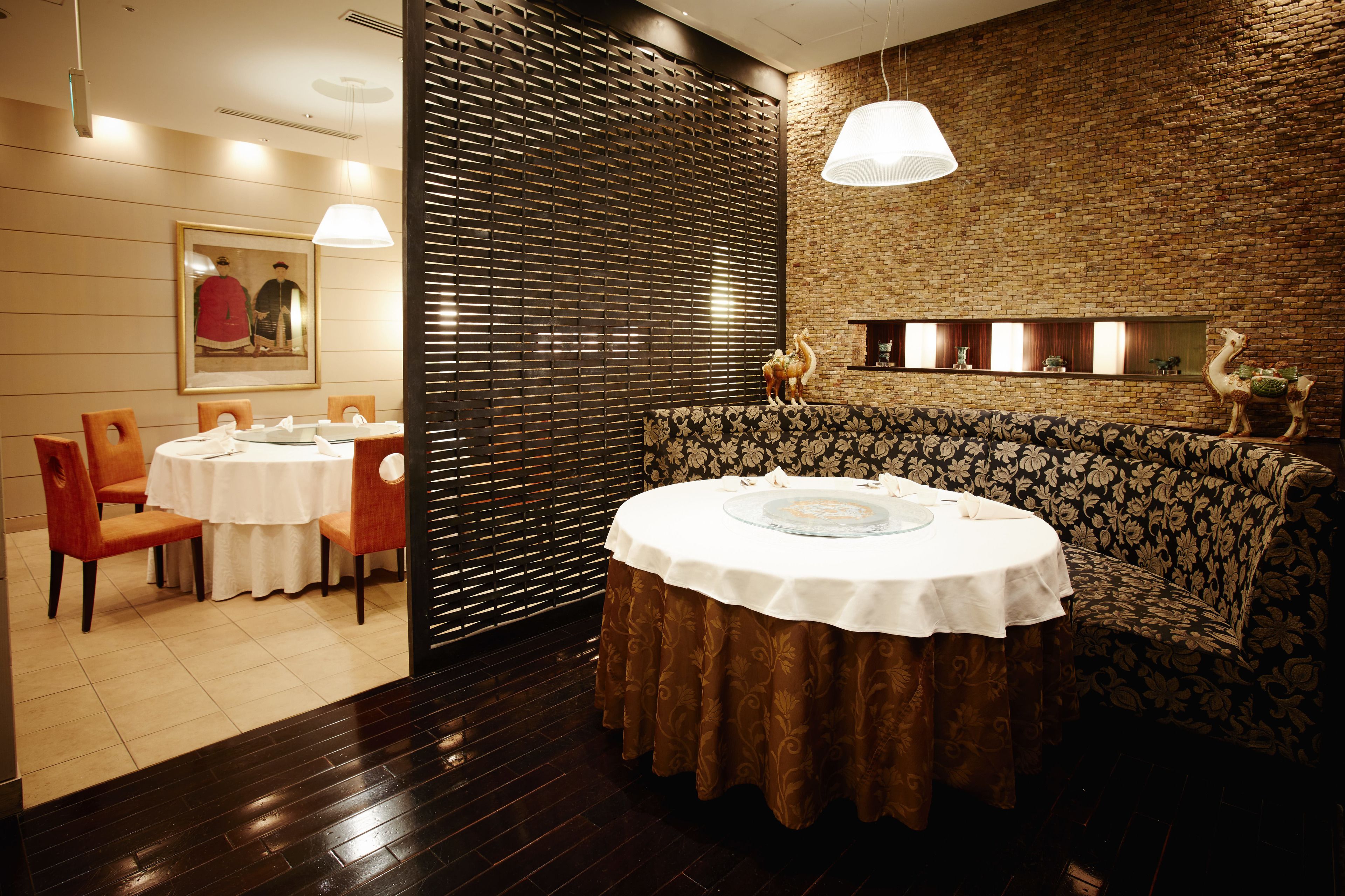 A restaurant with a round table, chairs, a patterned sofa, and a brick wall.