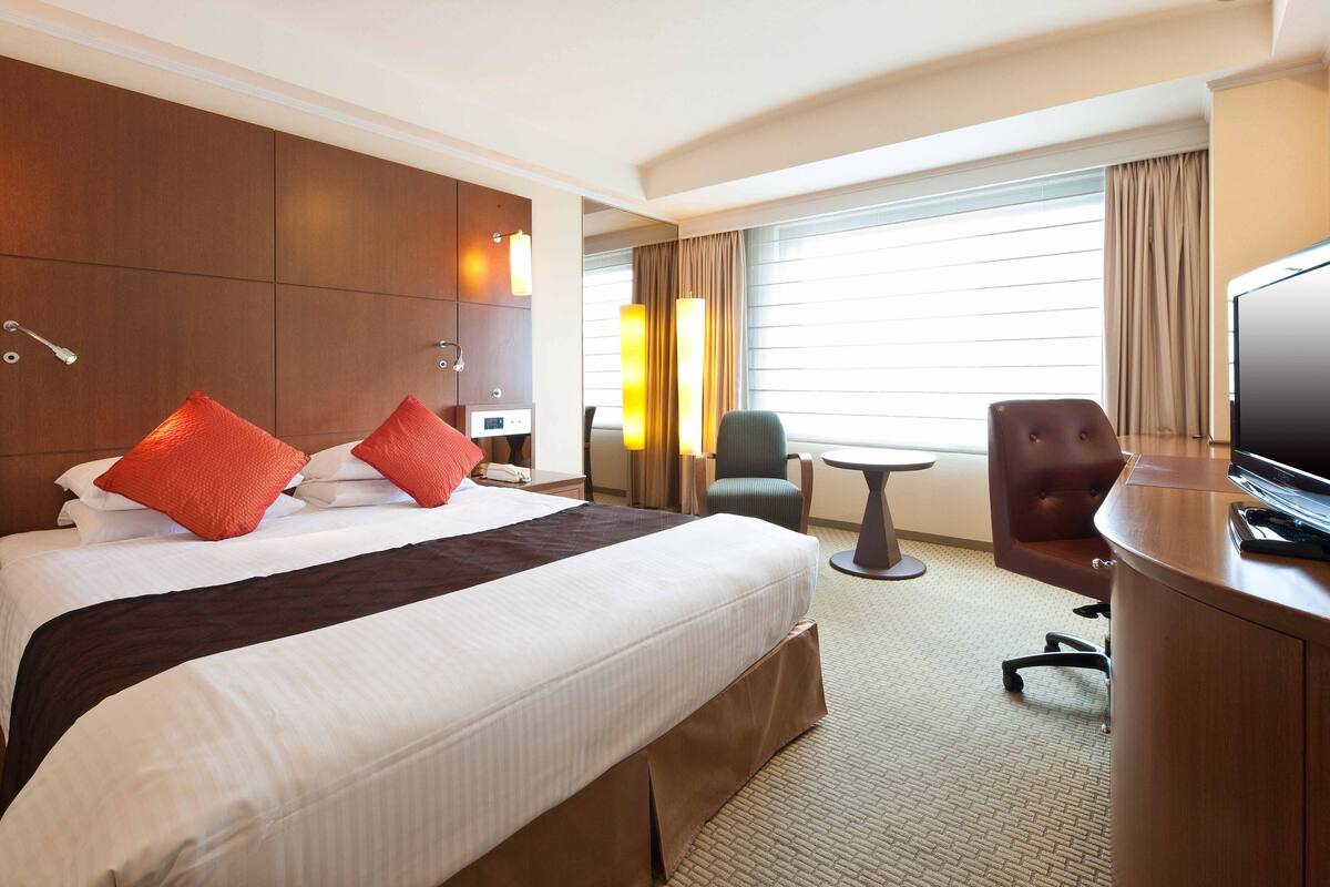 Ein Hotelzimmer mit einem großen Bett, einem Schreibtisch, einem Sessel und einem Fernseher.