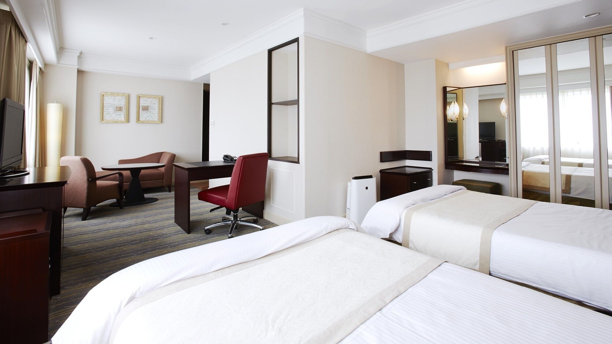 Une chambre d’hôtel avec deux lits, un bureau, une chaise, une télévision et un miroir.