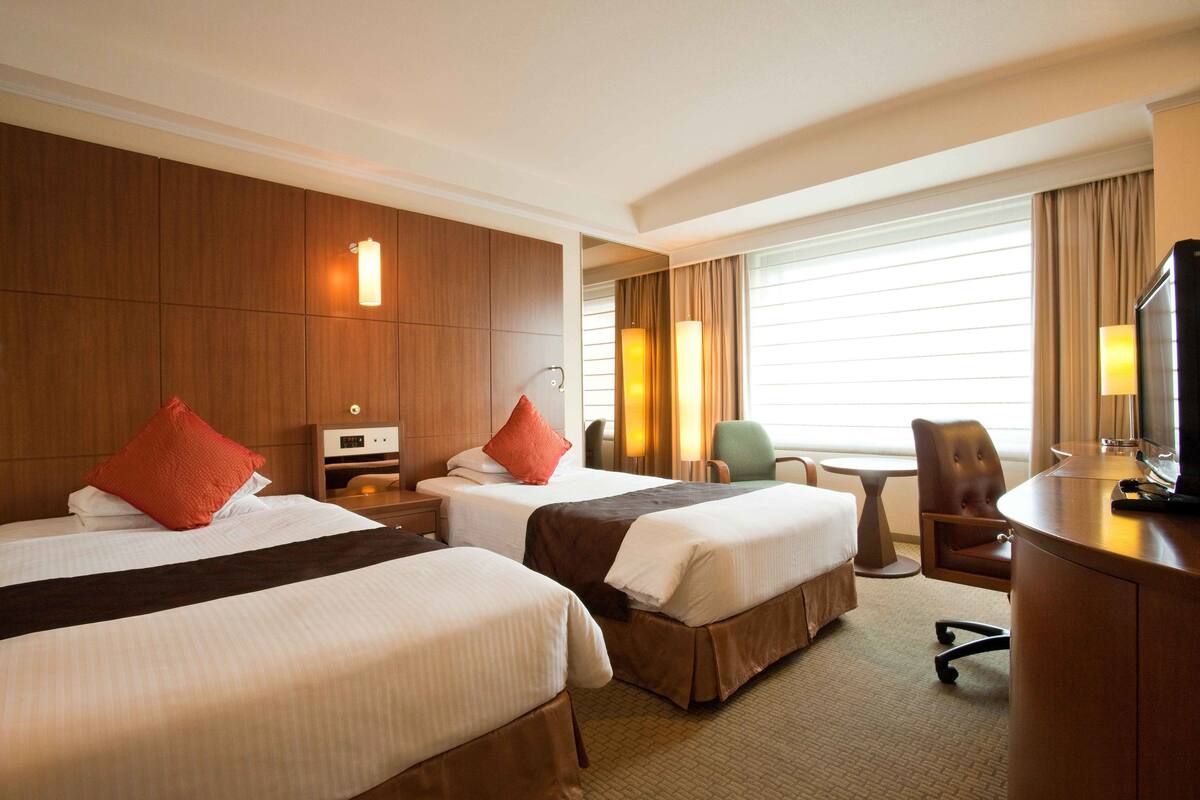 Ein Hotelzimmer mit zwei Betten, einem Schreibtisch, einem Sessel und einem Fernseher.