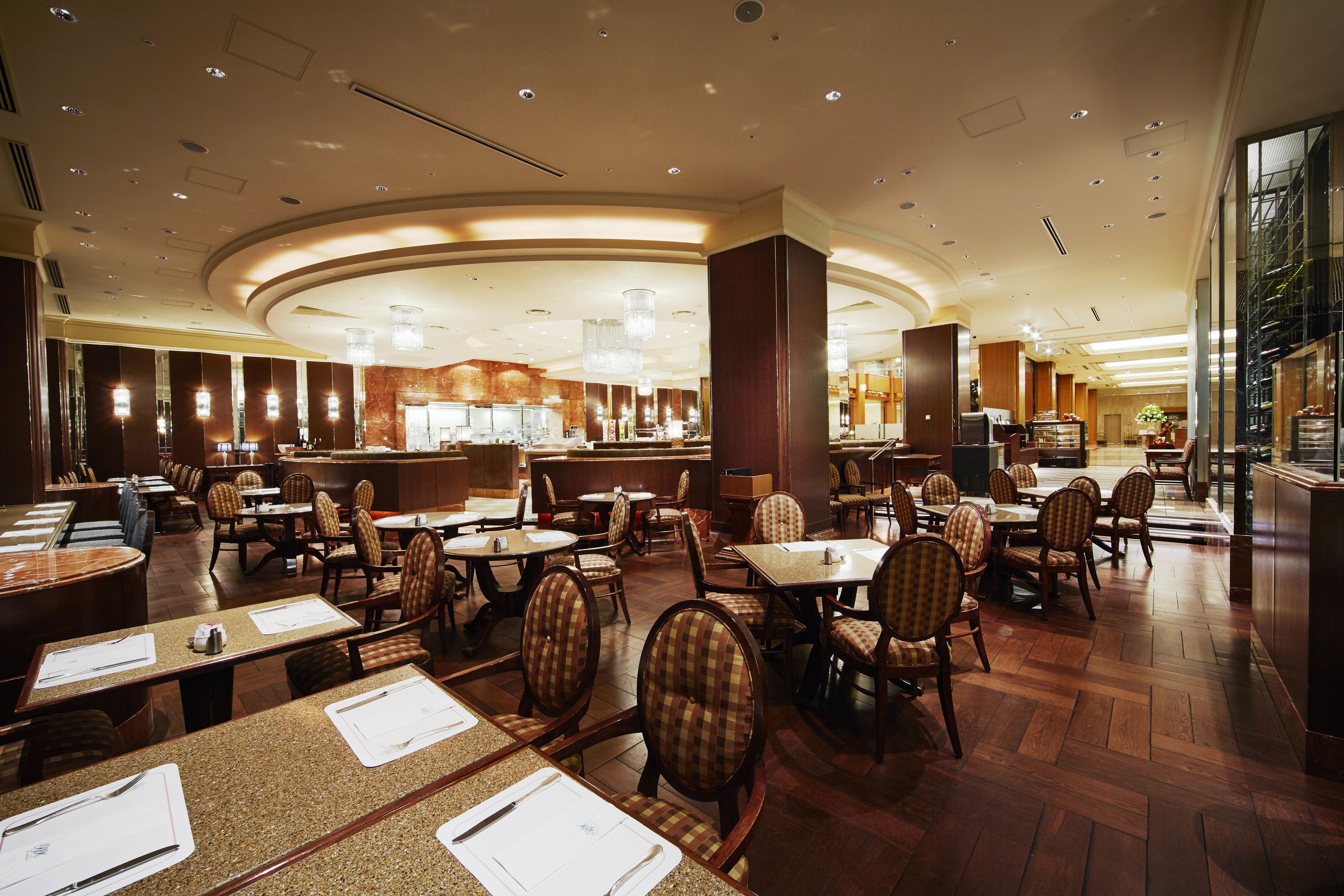 A spacious hotel dining area with multiple tables and chairs, a central bar, and a well-lit ceiling with recessed lighting.