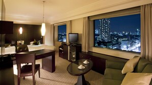 Ein Hotelzimmer mit Bett, Schreibtisch, Fernseher, Sofa und einem großen Fenster mit Blick auf die Stadt.