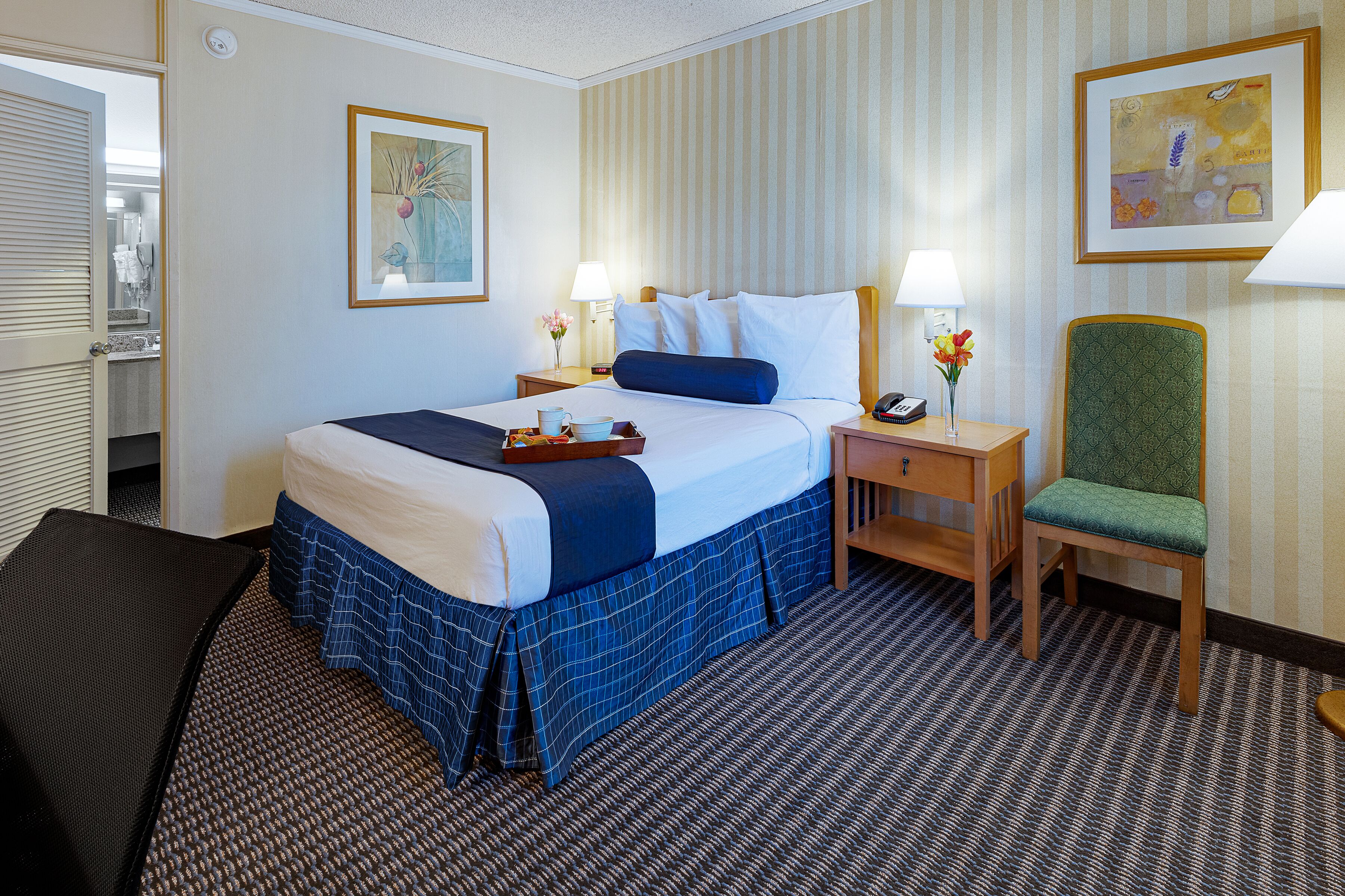 Una habitación de hotel con una cama, una silla, una mesita de noche, una lámpara y un cuadro en la pared.