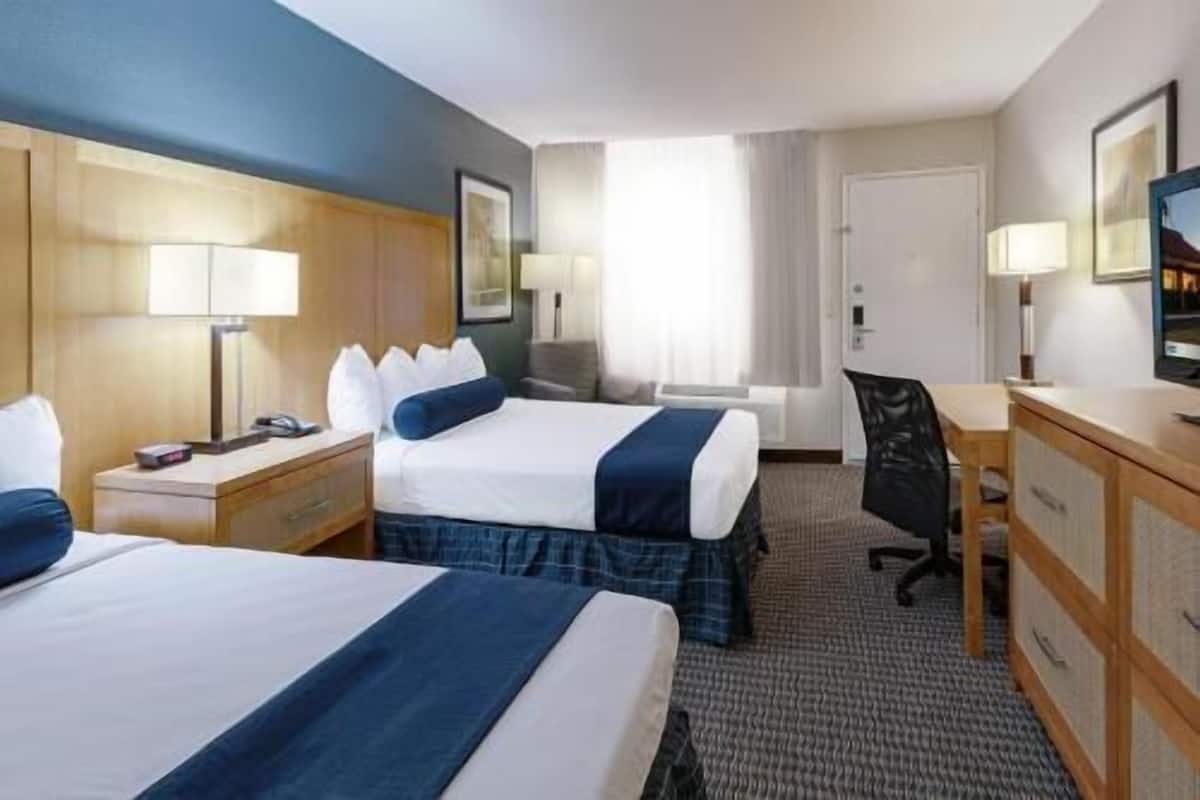 Ein Hotelzimmer mit zwei Betten, einem Schreibtisch, einem Stuhl, einem Schminktisch und einem Fernseher.