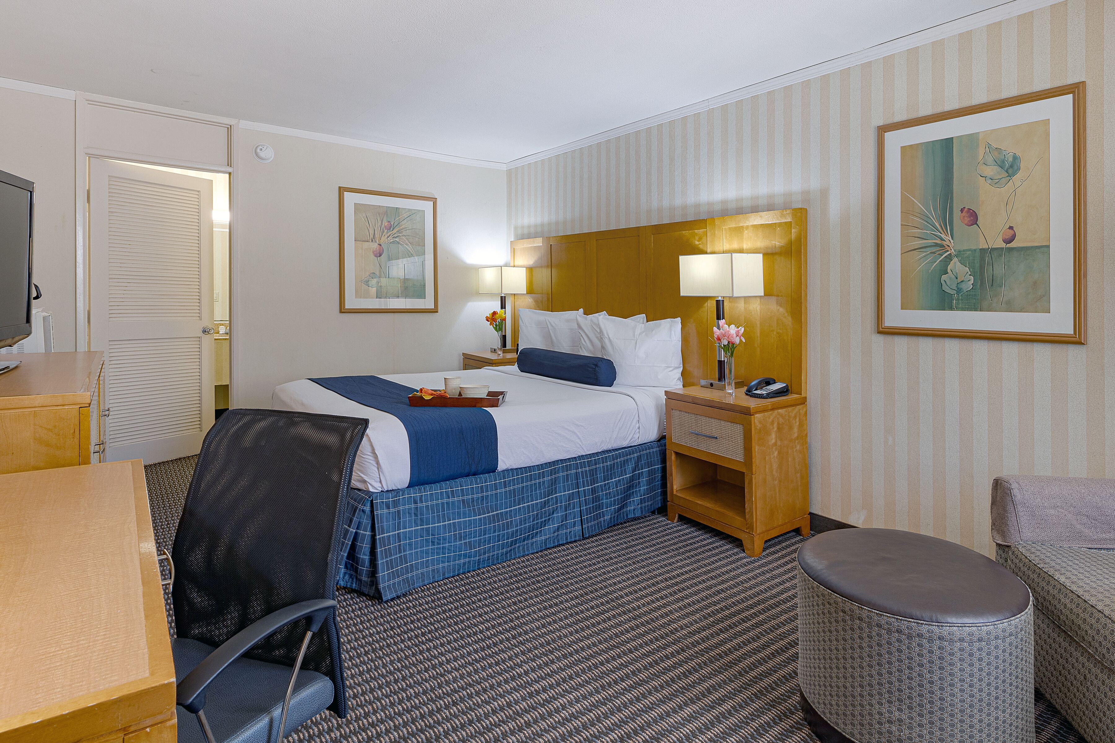 A hotel room with a bed, bedside table, lamp, chair, and a small table.