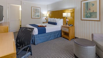 Una habitación de hotel con cama, mesita de noche, lámpara, silla y una pequeña mesa.
