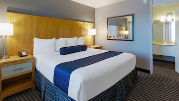 Une chambre d’hôtel avec un grand lit, deux tables de chevet, une commode, un miroir et un sol recouvert de moquette.
