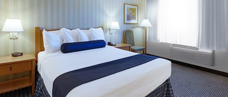 Une chambre d’hôtel avec un grand lit, deux tables de chevet, une chaise, une fenêtre avec des rideaux et un climatiseur fixé au mur.