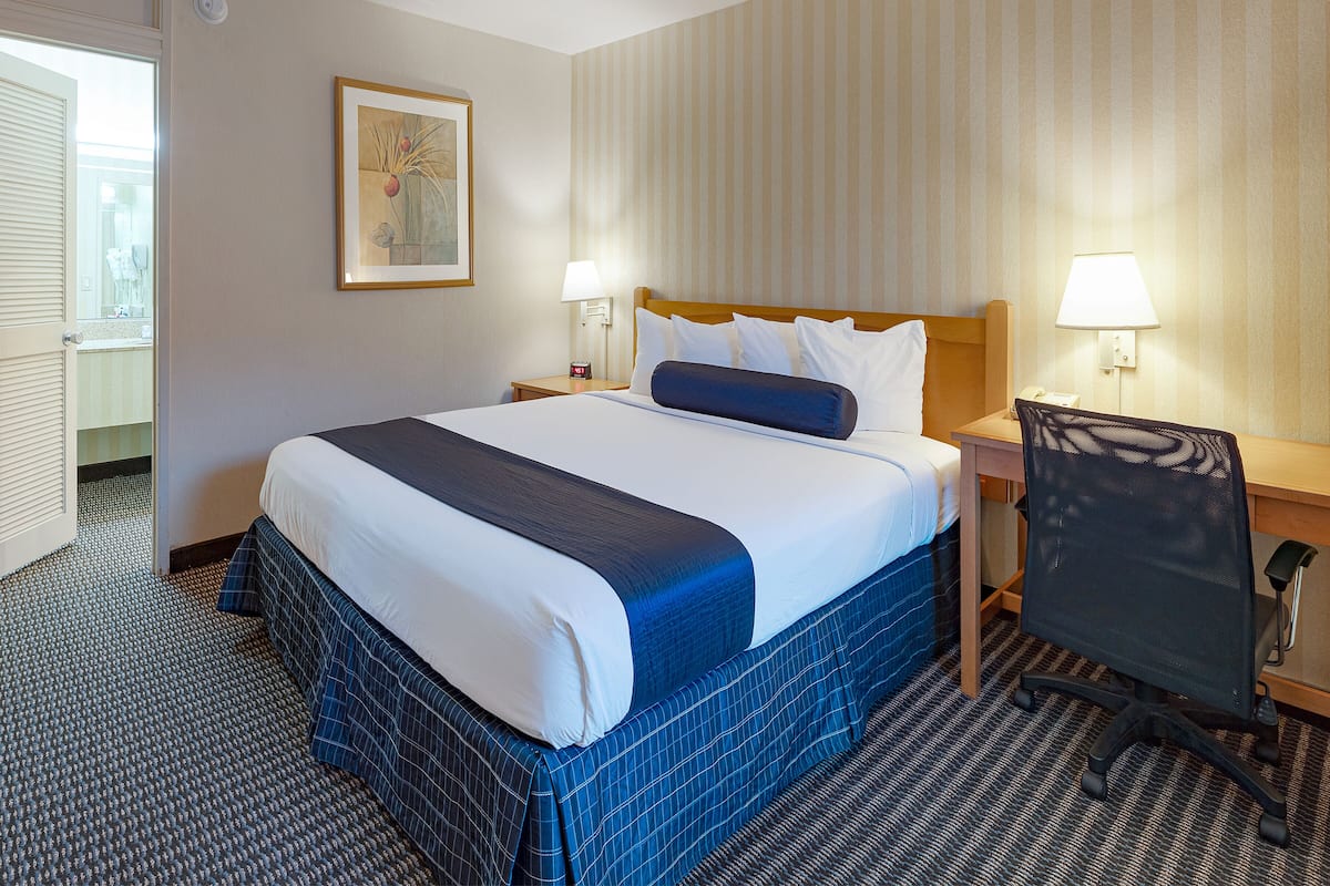 Ein Hotelzimmer mit einem großen Bett, zwei Nachttischlampen, einem Schreibtisch mit Stuhl und einem gerahmten Bild an der Wand.