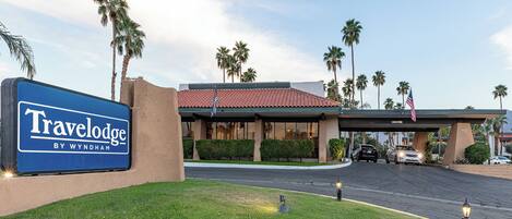 A Travelodge by Wyndham with a red-tiled roof, palm trees, and a clear sky.