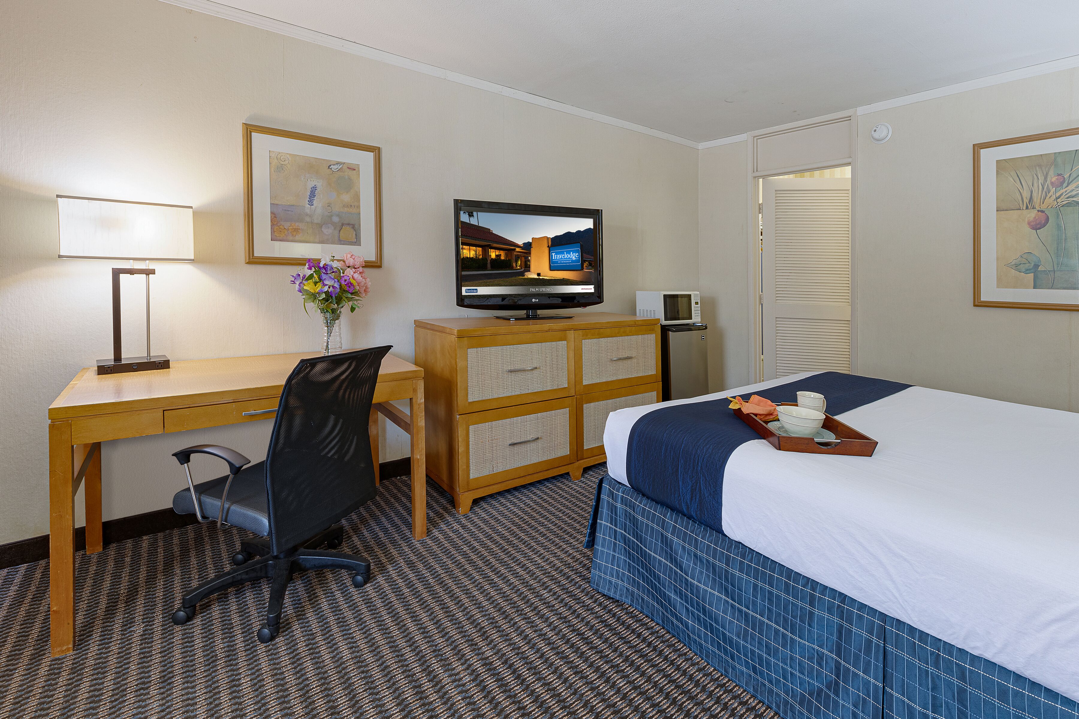 Een hotelkamer met een bed, bureau, stoel, televisie en een klein kastje.