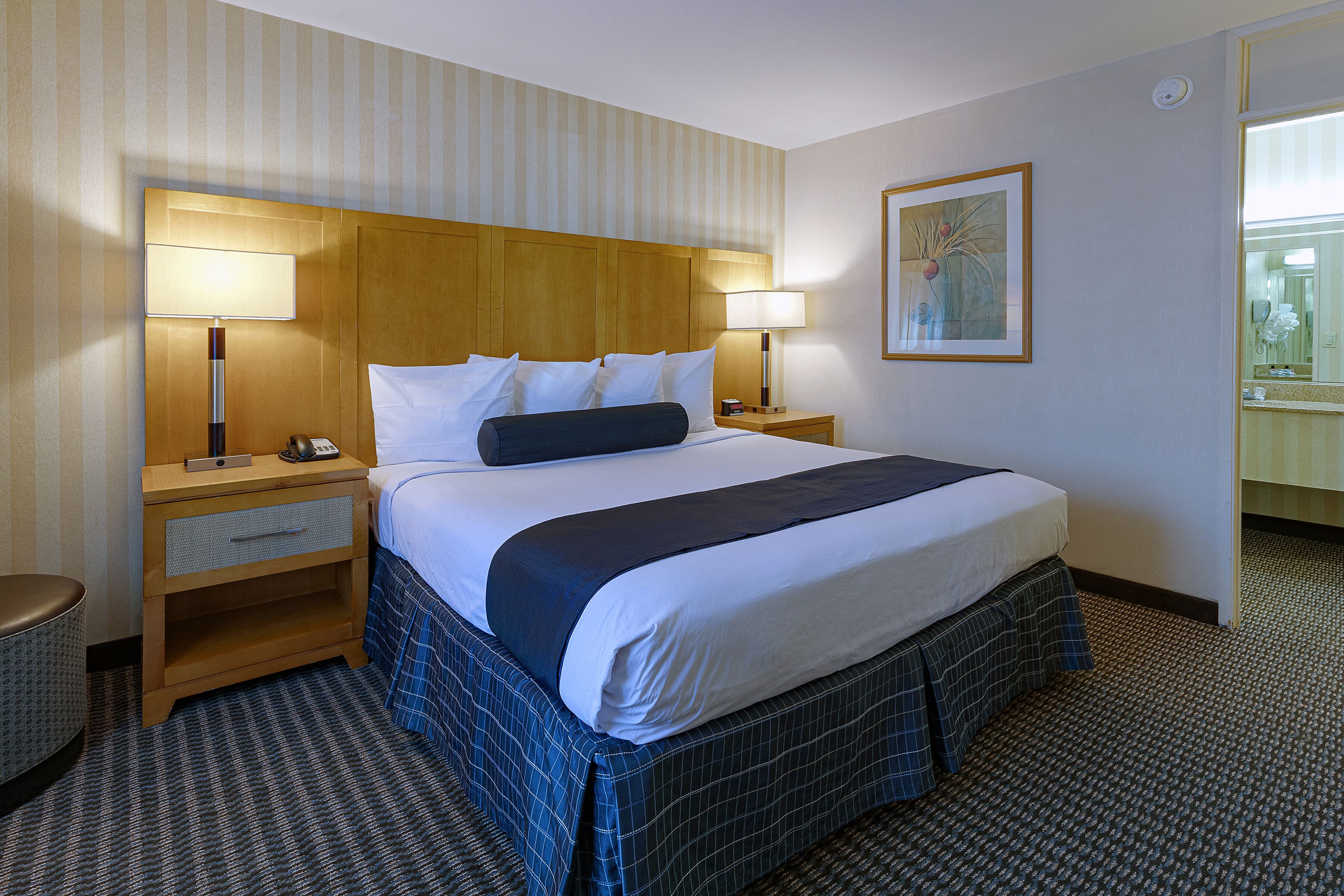 Ein Hotelzimmer mit einem großen Bett, zwei Nachttischen, einer Stehlampe, einem gerahmten Bild an der Wand und einem Teppichboden.