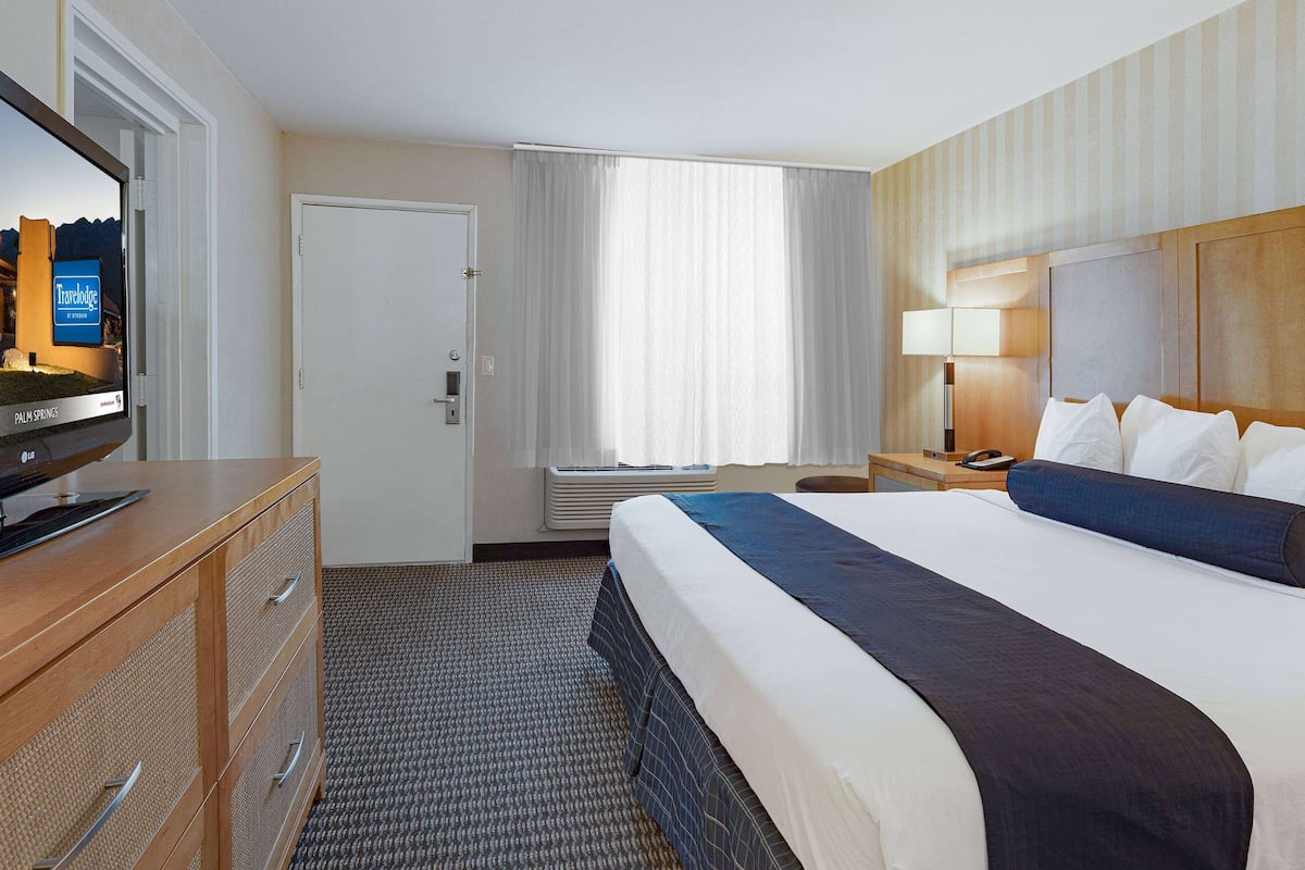 Ein Hotelzimmer mit Bett, Fernseher, Schreibtisch und einem Fenster mit Vorhängen.