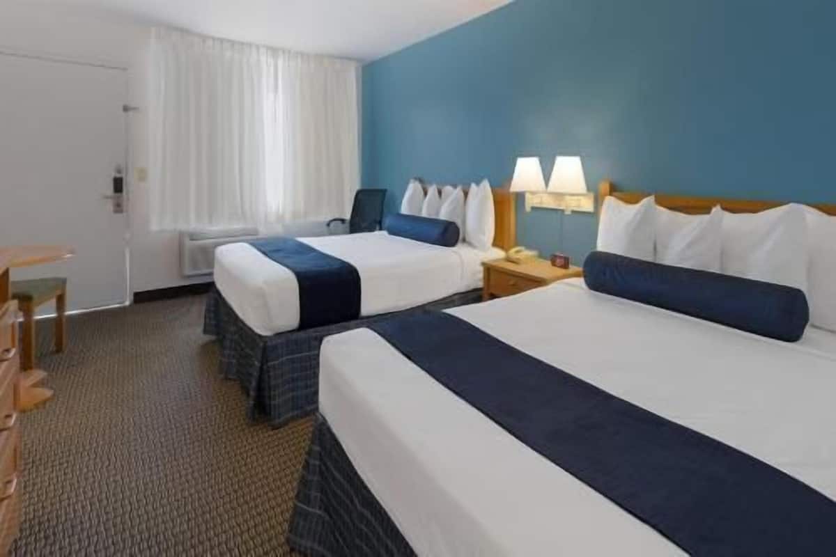 Ein Hotelzimmer mit zwei Betten, einem Schreibtisch, einem Stuhl und einem Fenster mit Vorhängen.