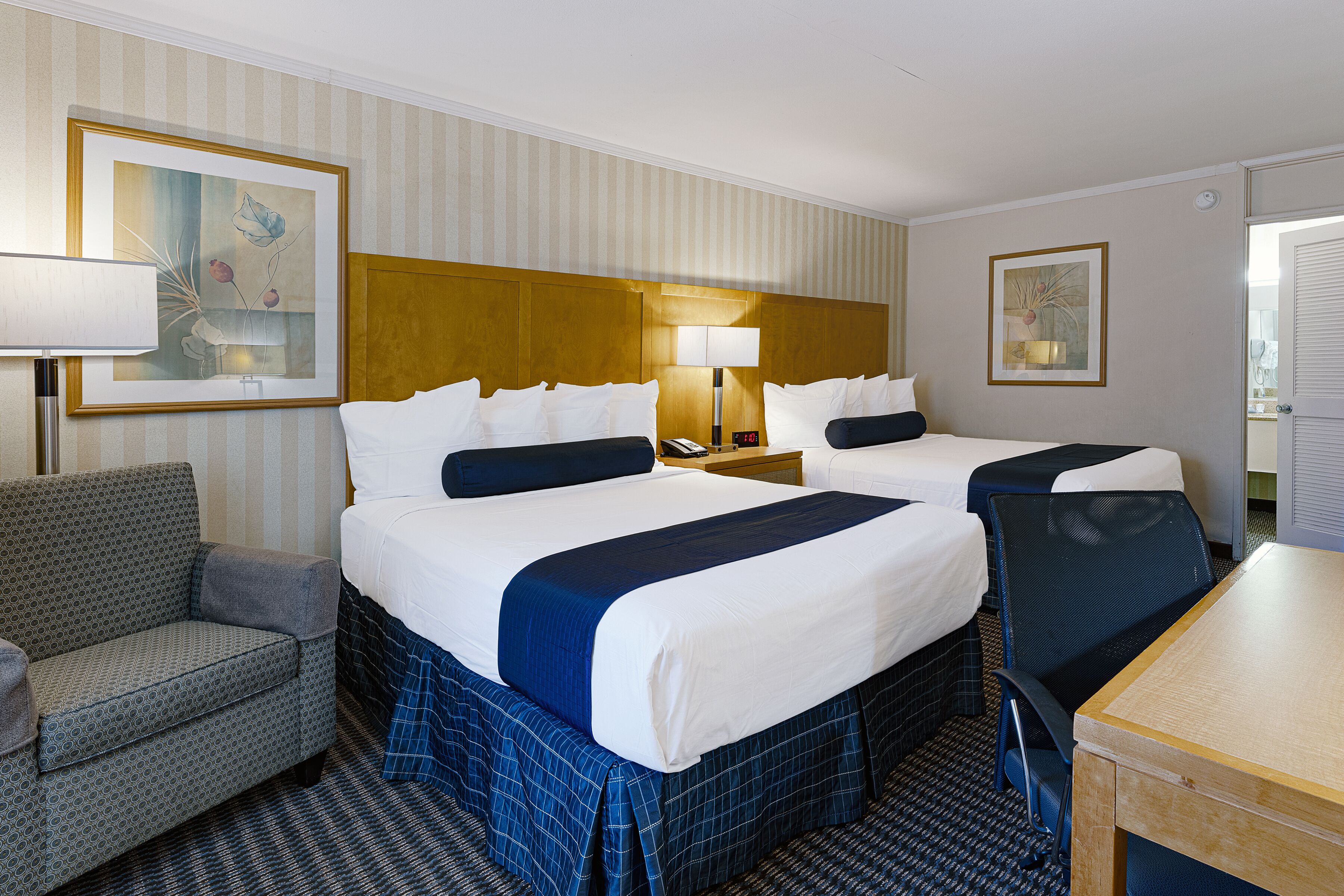 A hotel room with two beds, a sofa, a desk, and a lamp.