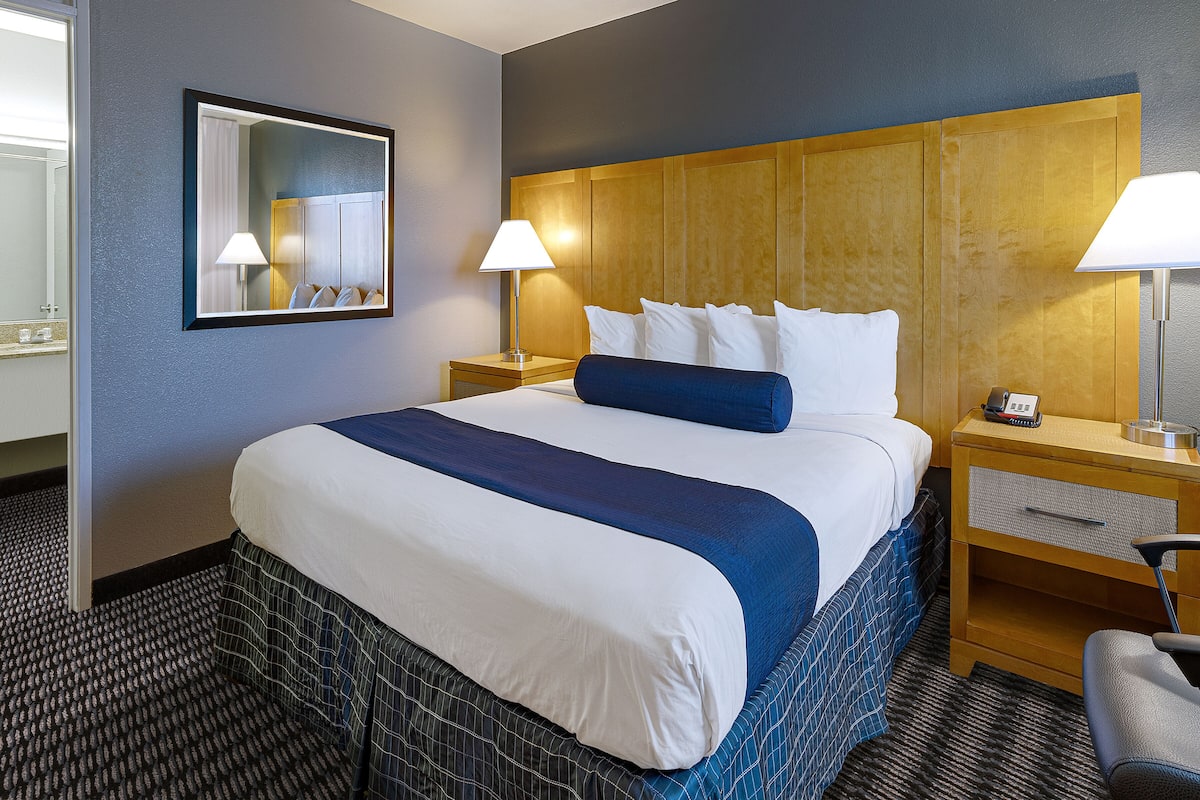 Ein Hotelzimmer mit einem großen Bett, zwei Nachttischen, einem Spiegel und einem Sessel.