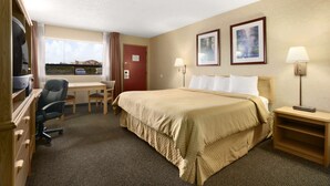 A hotel room with a large bed, a desk with a chair, a TV, and two framed pictures on the wall.