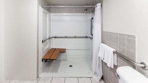 A wheelchair-accessible shower stall with a bench, grab bars, and a towel rack.