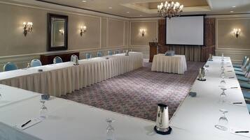Ett konferensrum med ett långt bord, stolar, en projektorduk och en talarstol.