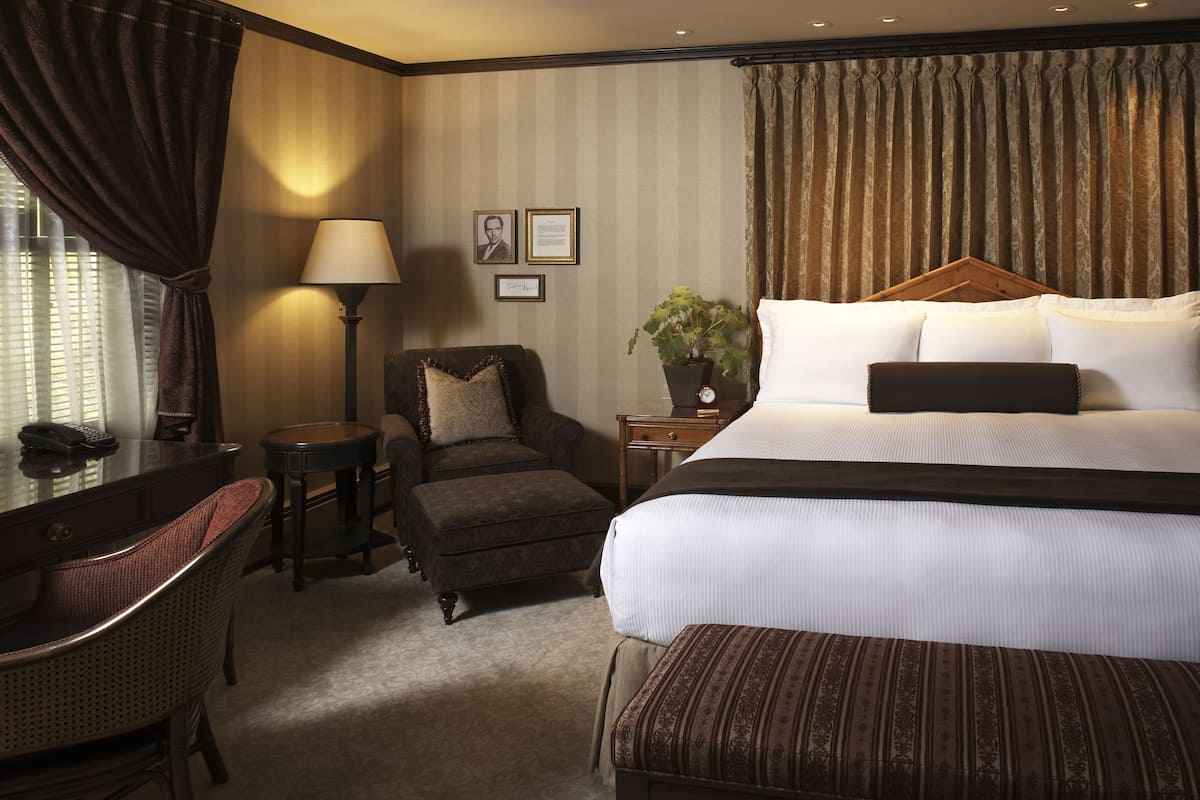 A hotel room with a large bed, a chair, a desk, and a lamp.