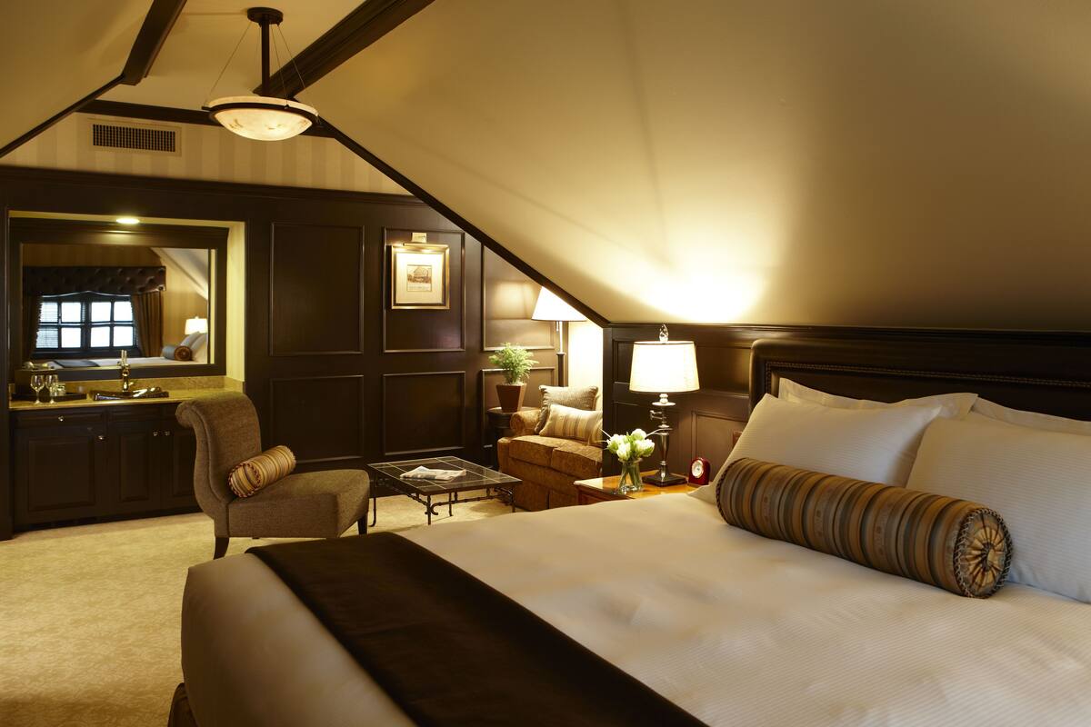 A hotel room with a large bed, a sitting area with a sofa and armchair, a small table, and a desk with a lamp.
