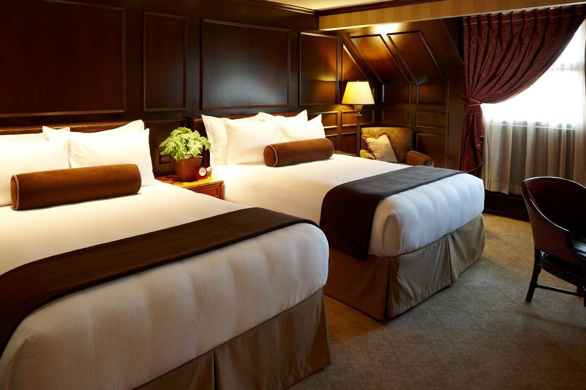 A hotel room with two beds, a nightstand with a lamp, a chair, and a potted plant.