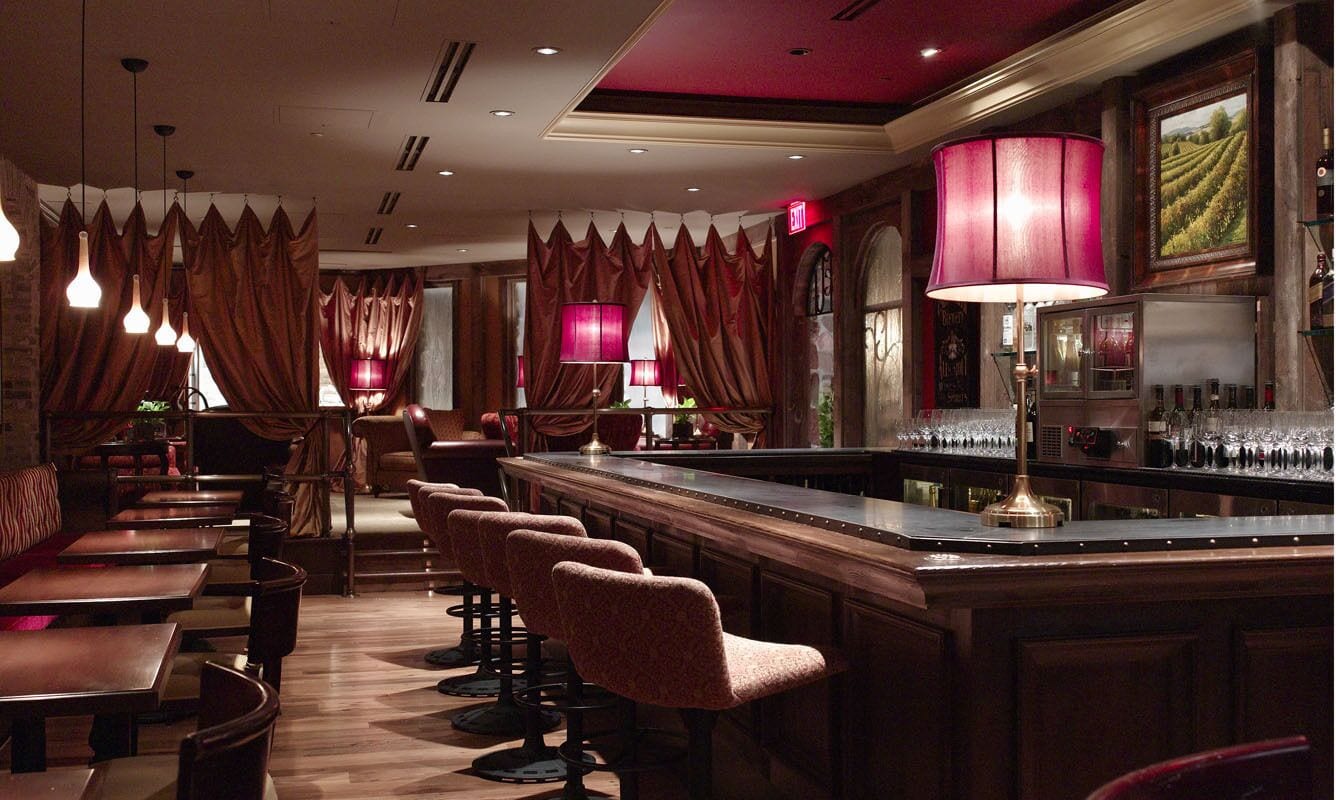 A bar area with a long counter, multiple bar stools, and a bar stocked with bottles.