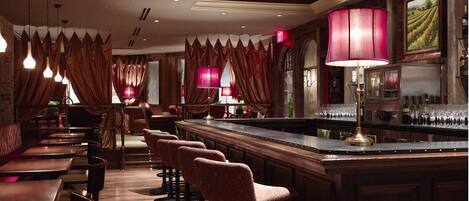 A bar area with a long counter, multiple bar stools, and a bar stocked with bottles.