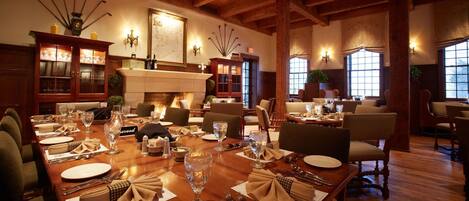 A dining area with wooden tables set for a meal, a fireplace, and a large map on the wall.