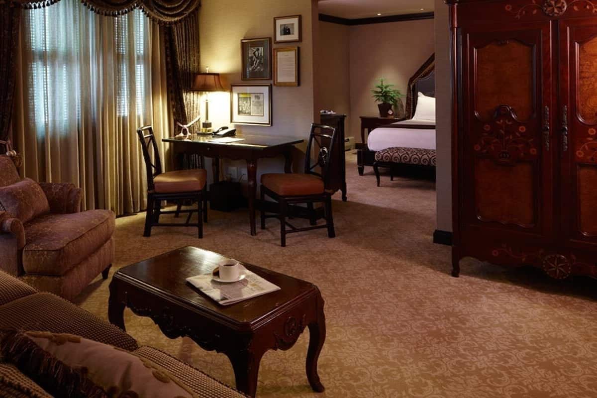 A traditional hotel room with a sofa, armchair, dining table, and a bed.