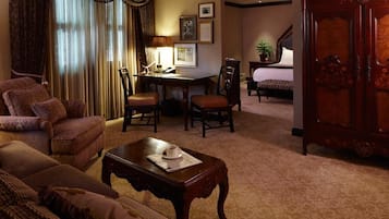 A traditional hotel room with a sofa, armchair, dining table, and a bed.