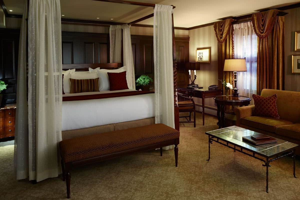 A traditional room with a four-poster bed, a sofa, a bench, and a coffee table.
