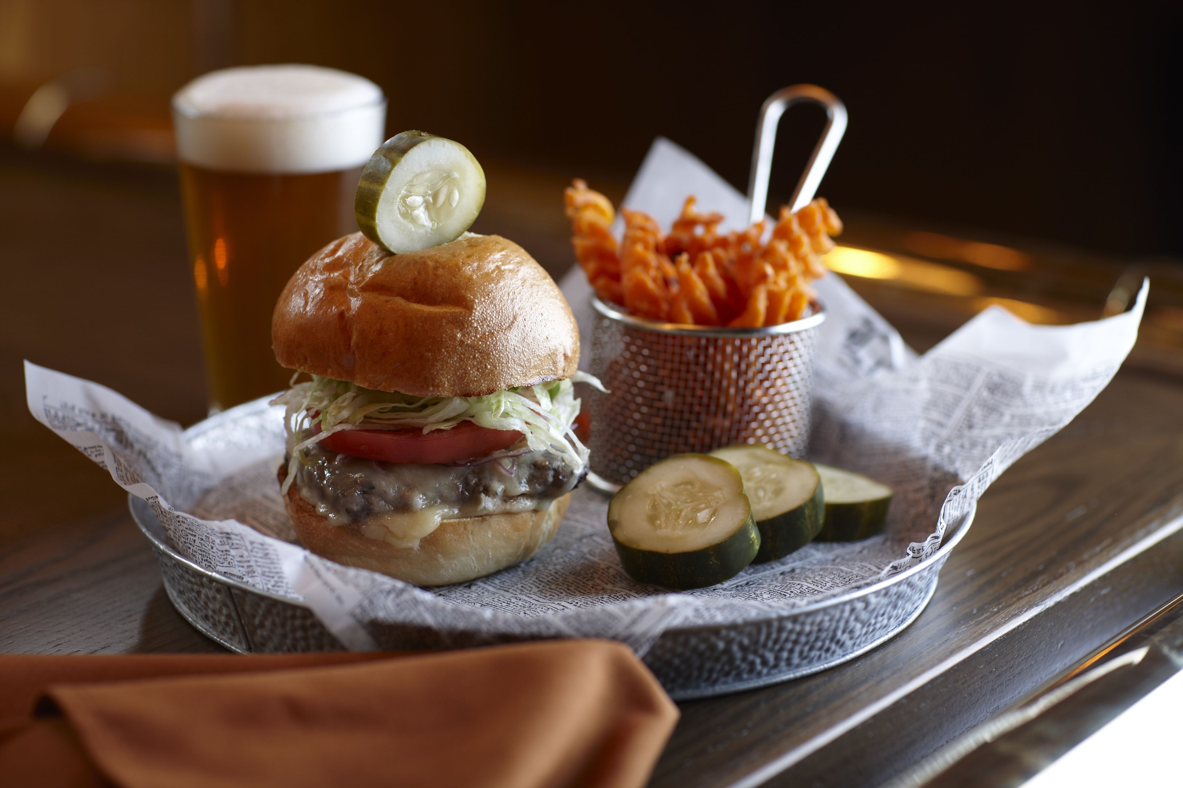 A burger with a pickle, fries, and a drink on a table.