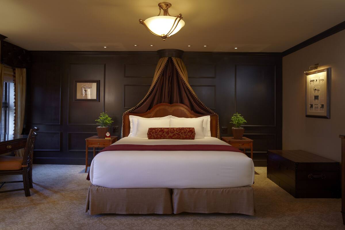 A large bed with a canopy, two bedside tables with lamps, a chair, and a small cabinet.