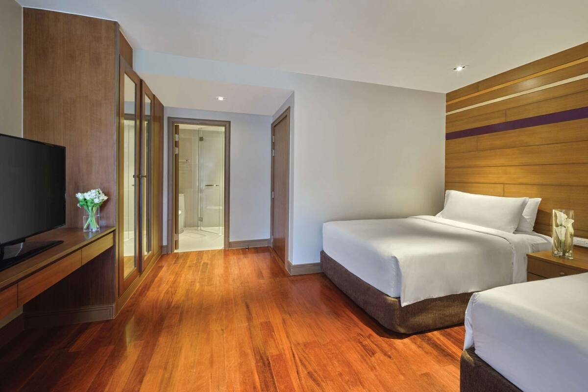 A hotel room with a wooden floor, a TV, a bed, and a wardrobe.