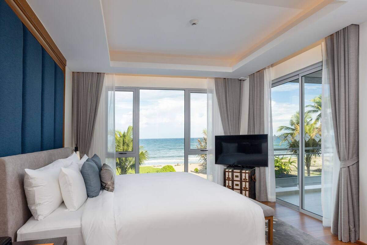 A hotel room with a large bed, a flat-screen TV, and a view of the ocean.