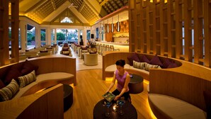 A spacious lounge area with wooden furniture, a bar, and large windows offering a view of the outdoors. - Angsana Laguna Phuket (Choeng Thale)