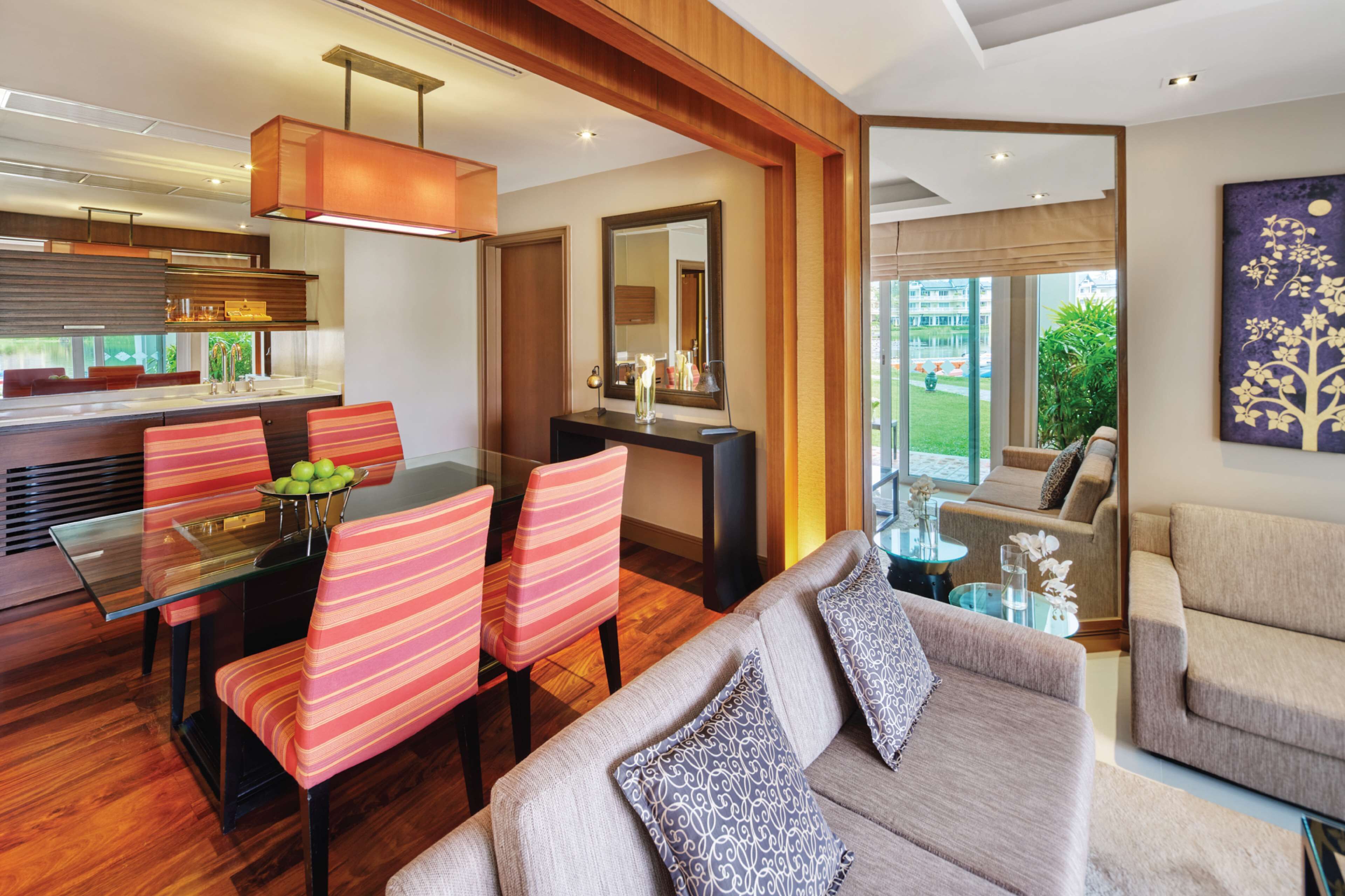 Una sala de estar moderna con una mesa de comedor de vidrio, sillas a rayas, un sofá color beige y un ventanal con vistas al exterior.
