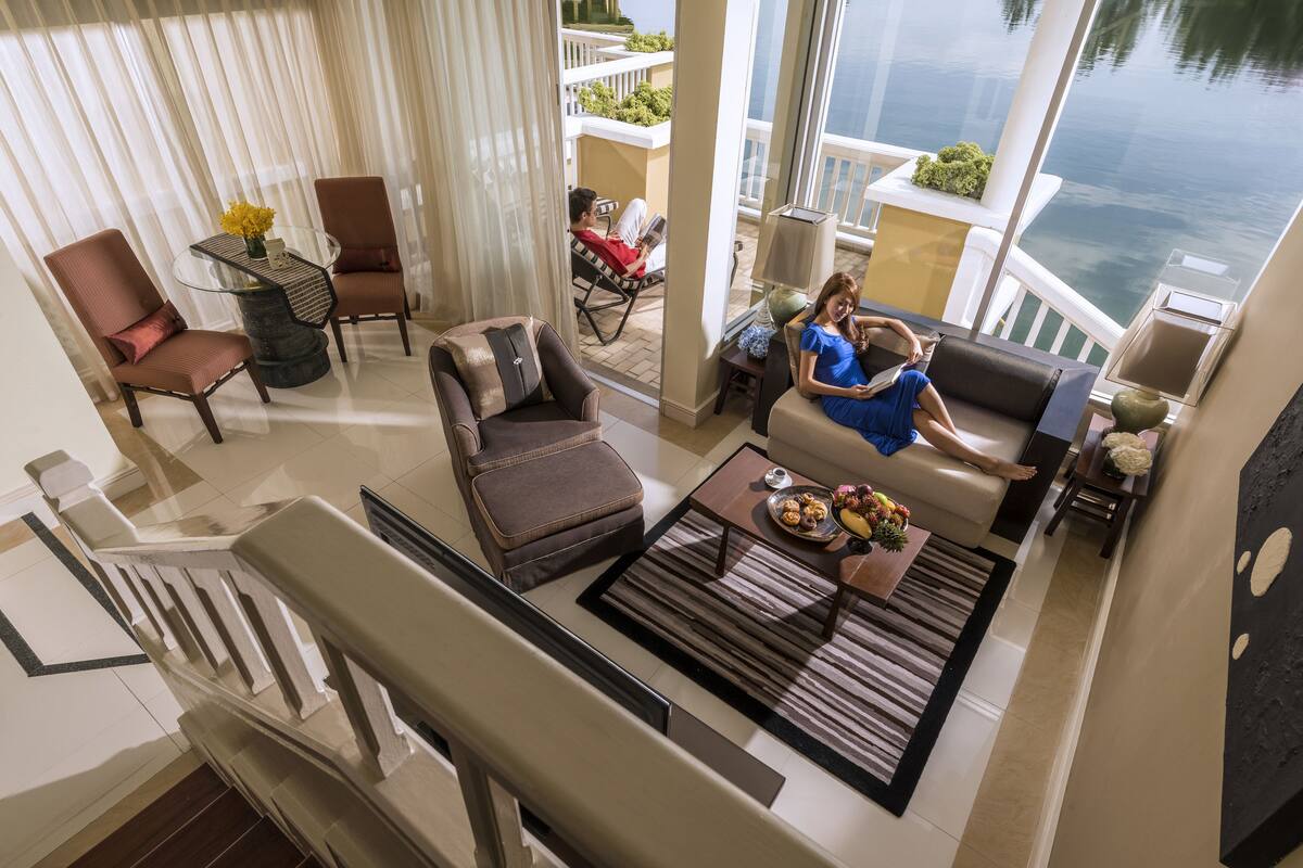 A spacious living area with a balcony overlooking a body of water, furnished with modern seating and a coffee table.