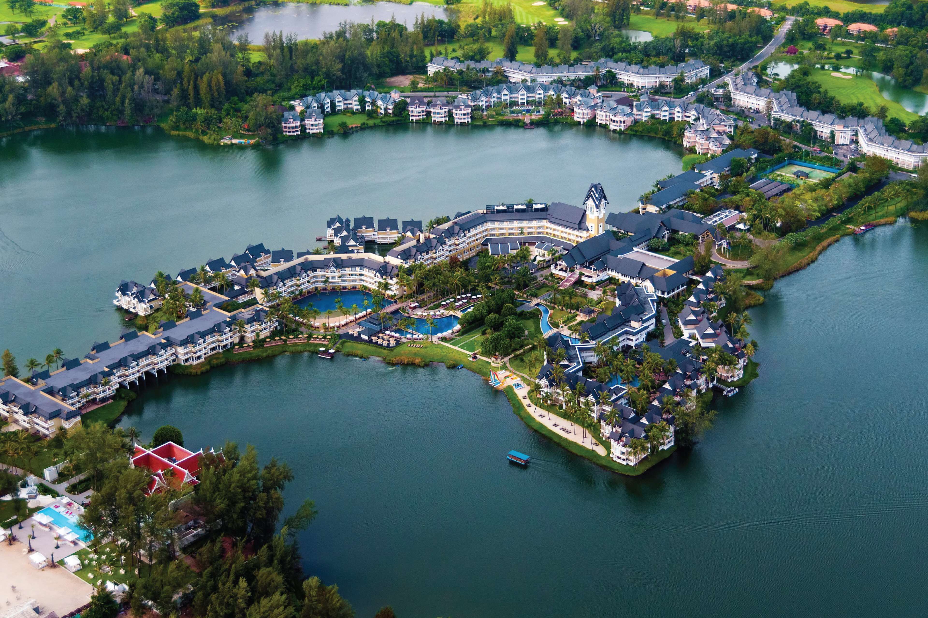 An aerial view of a lakeside resort with multiple buildings, a central tower, and a swimming area.