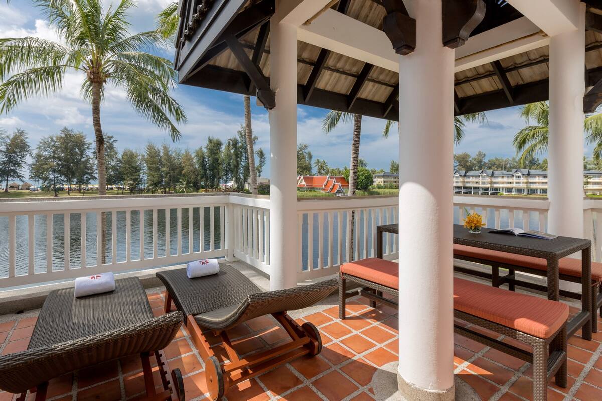A covered outdoor area with wicker furniture, a table with a book, and a view of a water body and buildings in the background.