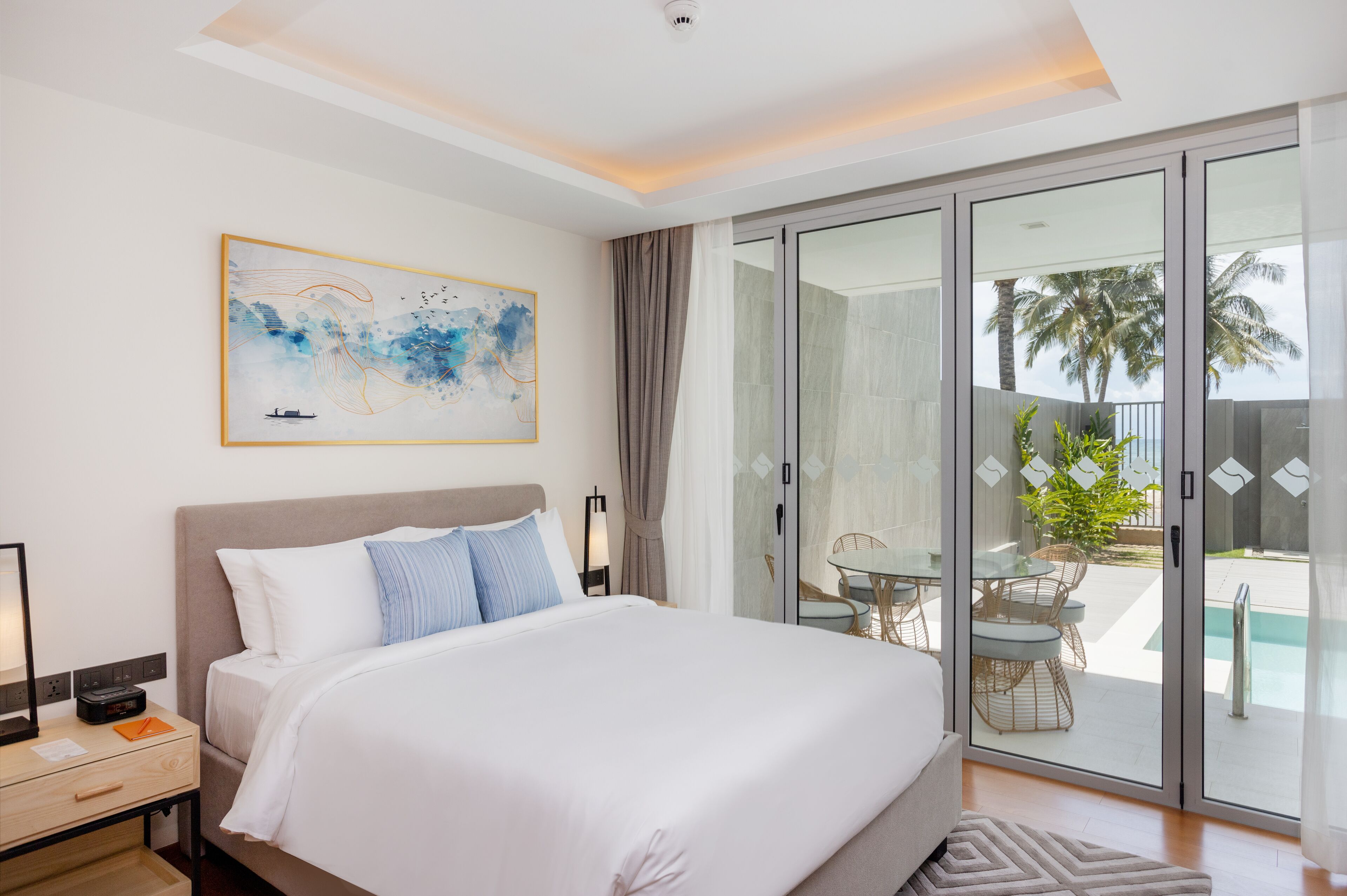 Una camera d'albergo moderna con un letto grande, una porta vetrata che dà su un balcone con piscina e un quadro appeso al muro.