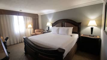 A hotel room with a large bed, two bedside tables with lamps, a chair, and a window with curtains.