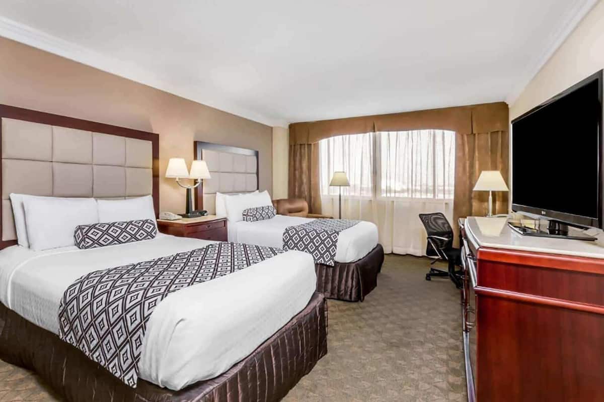 Een hotelkamer met twee bedden, een bureau, een televisie en een raam met gordijnen.